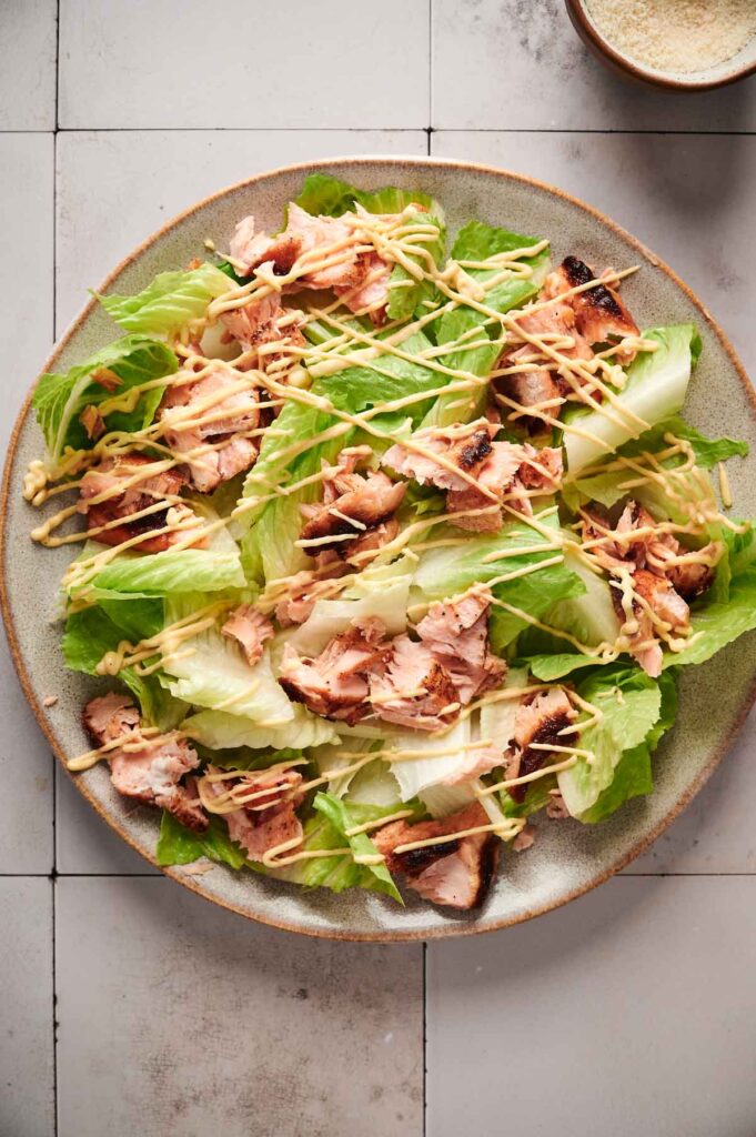 A salmon Caesar salad graces the tiled surface, featuring romaine lettuce topped with flaked grilled salmon and drizzled with a creamy dressing.