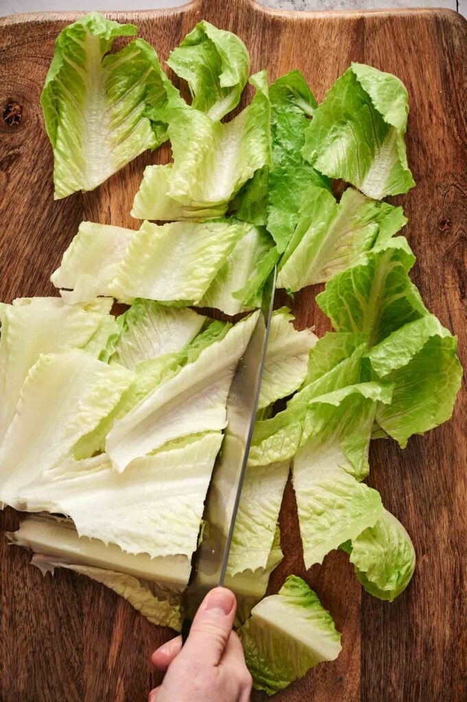 Hand chopping fresh green and white lettuce leaves for a delightful salmon Caesar salad on a wooden cutting board.
