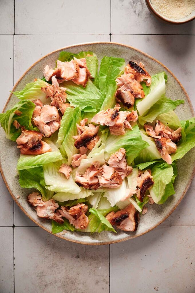 A plate of succulent salmon Caesar salad with grilled salmon pieces elegantly arranged over crisp romaine lettuce on a tiled surface.