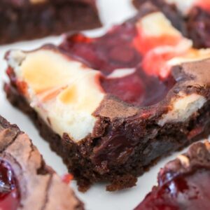 A close-up of Strawberry Cheesecake Brownies with a swirl of cherry filling on top, cut into squares and arranged on a white surface.