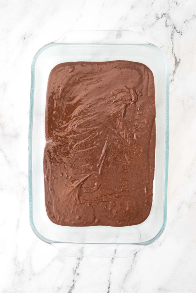 A glass baking dish filled with rich Strawberry Cheesecake Brownies batter sits on a white marble surface.