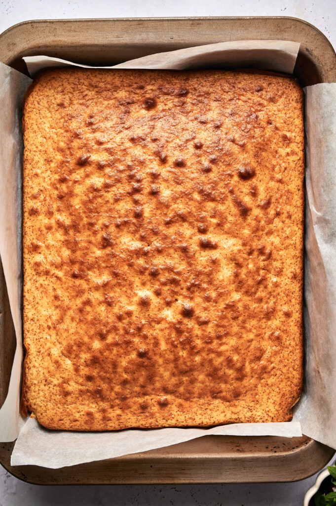 A golden-brown Strawberry Poke Cake sits in a parchment-lined baking pan, viewed from above.