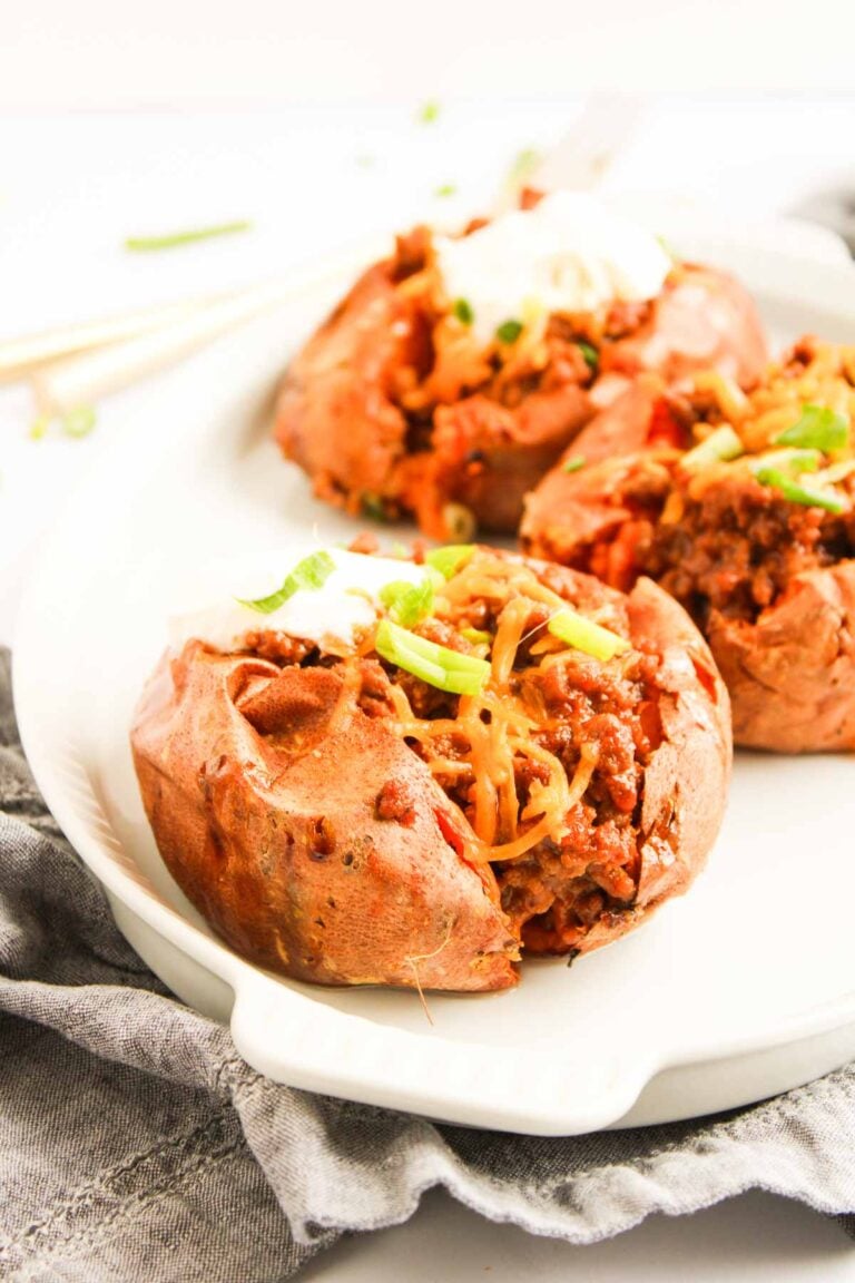 Baked sweet potatoes split open and filled with Sweet Potato Sloppy Joes mixture, shredded cheese, and a dollop of sour cream, served on a white plate.