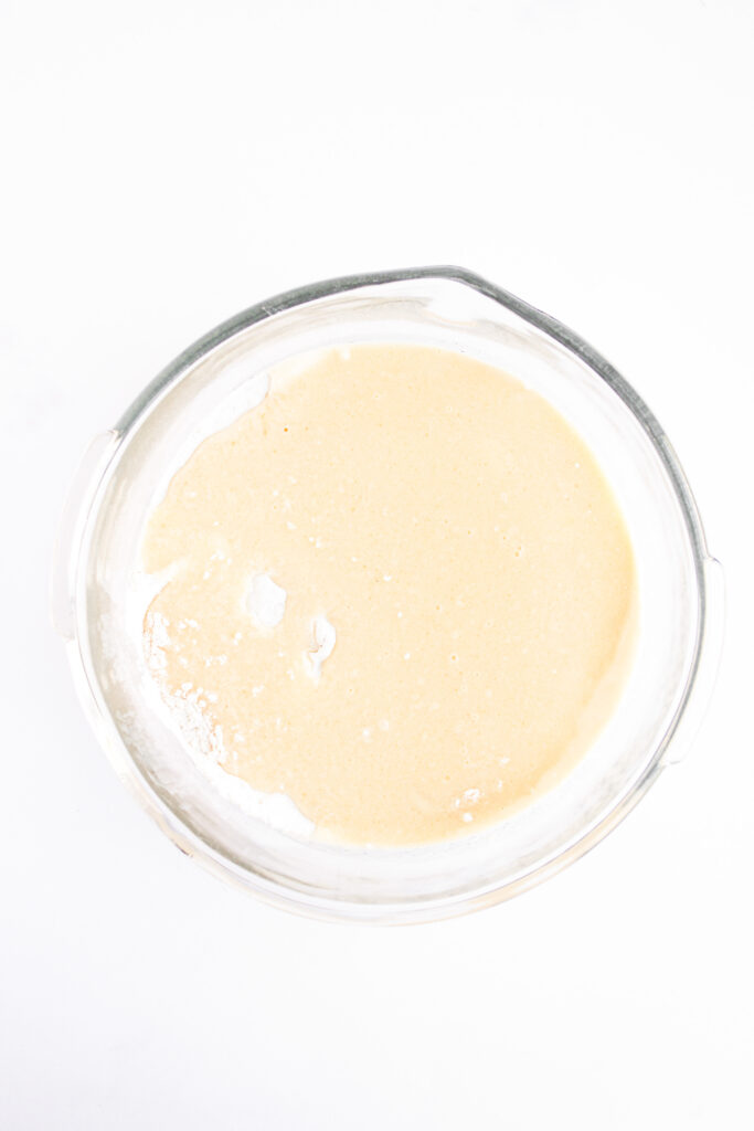 A glass mixing bowl filled with smooth, light beige 4th of July Muffins batter on a white background.