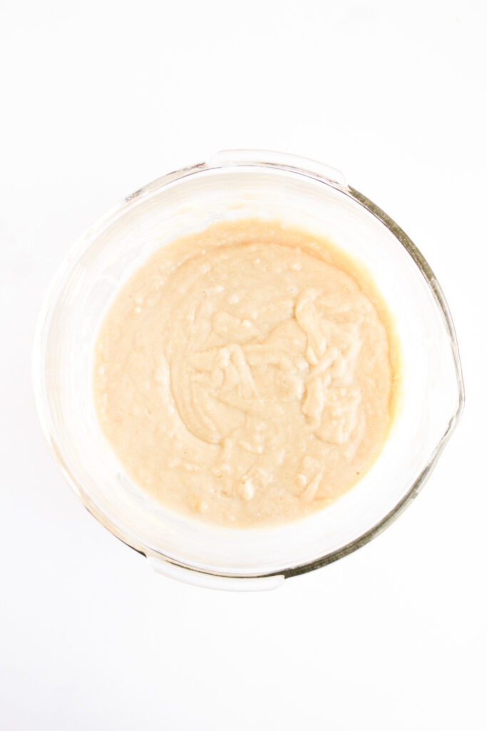 A glass mixing bowl containing smooth, pale 4th of July Muffins batter sits on a white background.
