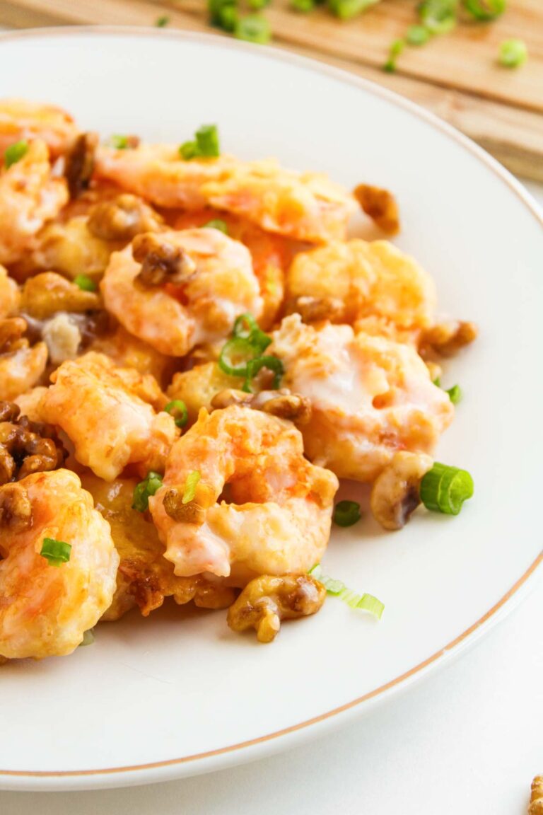 A plate of Air Fryer Honey Walnut Shrimp garnished with chopped green onions and candied walnuts, served on a white dish.