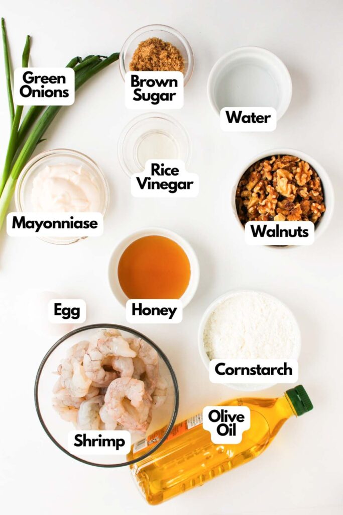 Top-down view of ingredients for Air Fryer Honey Walnut Shrimp in bowls and containers, including green onions, brown sugar, water, walnuts, rice vinegar, mayonnaise, egg, honey, cornstarch, shrimp, and olive oil.