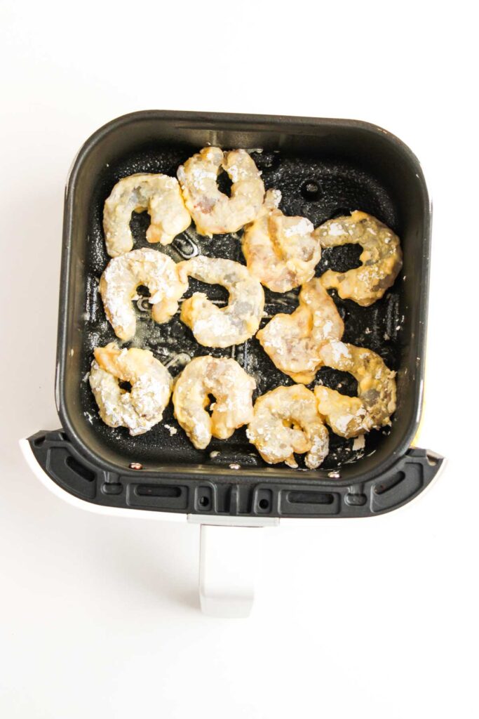 Raw battered shrimp arranged in a single layer inside an air fryer basket, ready to be cooked for delicious Air Fryer Honey Walnut Shrimp.