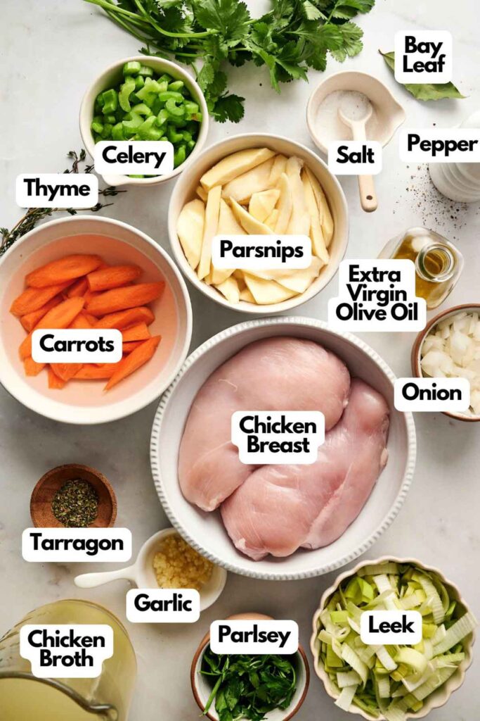 Assorted ingredients for a chicken recipe arranged on a countertop, including chicken breast, vegetables, herbs, spices, olive oil, and chicken broth&mdash;perfect for preparing delicious homemade Chicken Soup&mdash;each labeled.