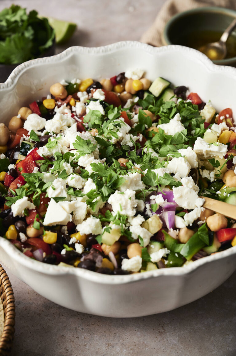 A bowl of cowboy caviar-inspired chopped salad with chickpeas, corn, black beans, tomatoes, cucumbers, red onions, herbs, and crumbled feta cheese.