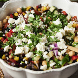 A bowl of cowboy caviar-inspired chopped salad with chickpeas, corn, black beans, tomatoes, cucumbers, red onions, herbs, and crumbled feta cheese.