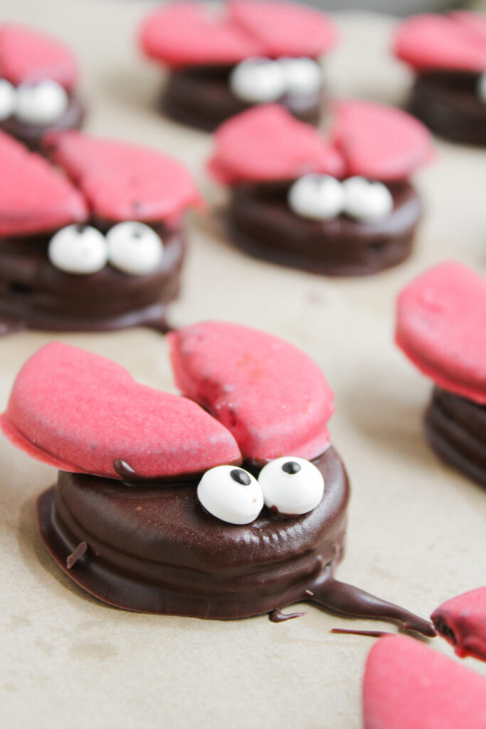 Chocolate cookies decorated with red cookie halves and candy eyes to resemble crabs, inspired by Ladybug Chocolate Covered Oreos, are arranged on a baking sheet.