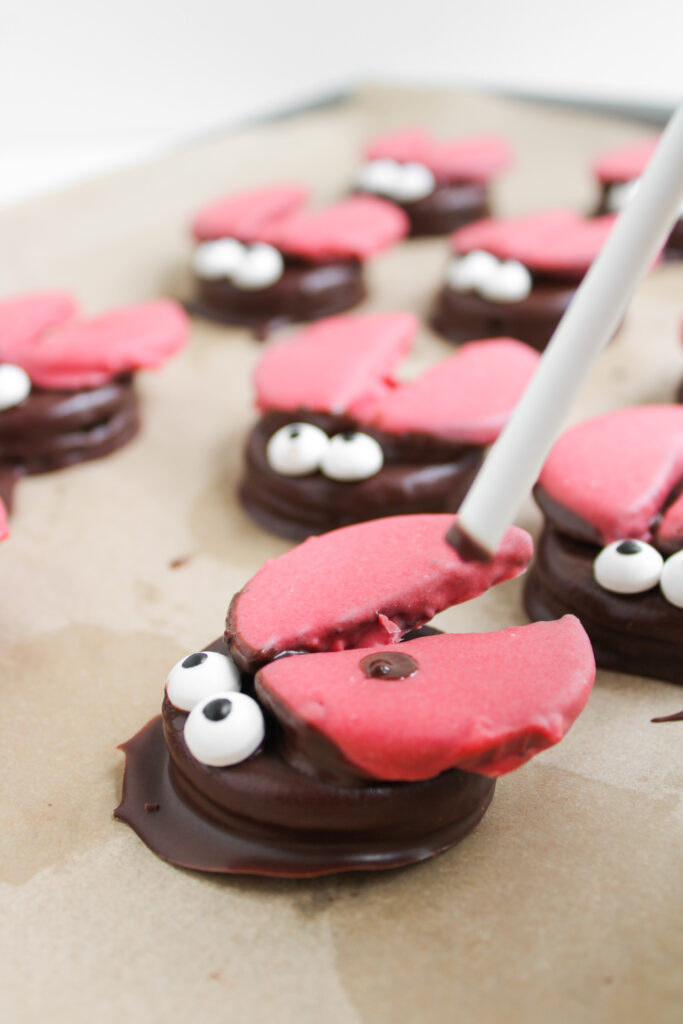 Chocolate cookies topped with pink cookie halves shaped like crab claws and decorated with candy eyes—these delightful treats are inspired by Ladybug Chocolate Covered Oreos, arranged on parchment paper for a whimsical presentation.