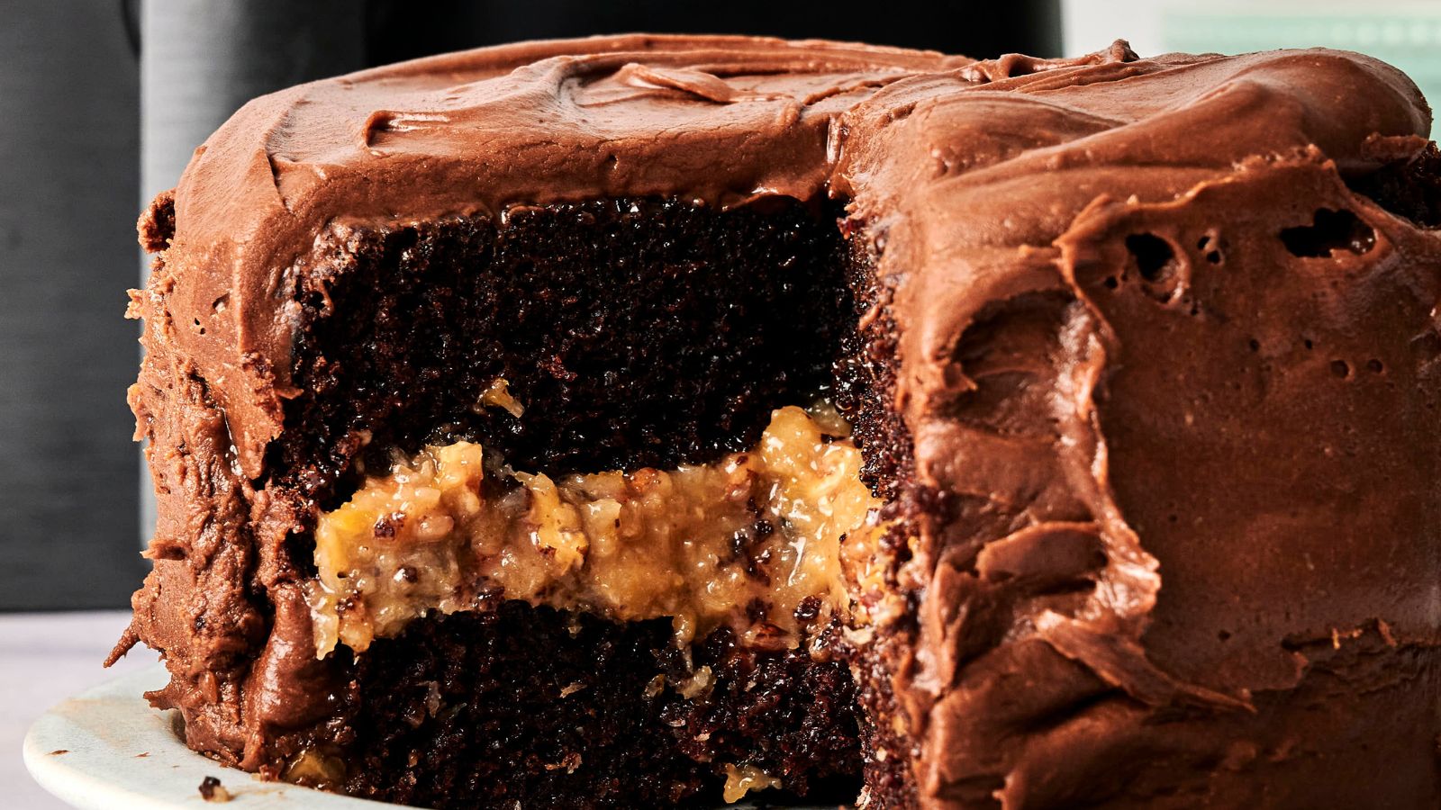 A chocolate layer cake with a slice removed, showing a caramel and coconut filling, and covered with chocolate frosting.