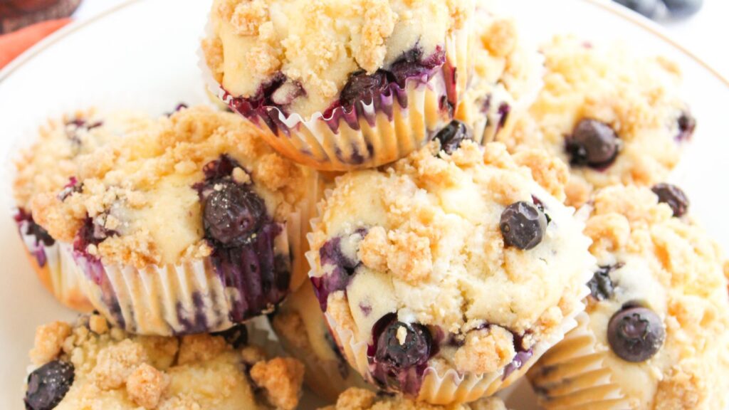 A plate of blueberry muffins topped with crumbly streusel, with visible whole blueberries and golden brown topping.