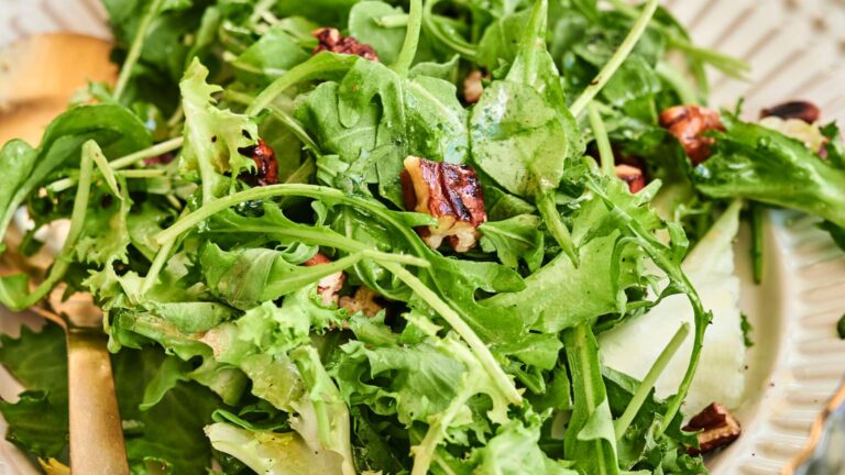 A close-up of a fresh green salad with arugula, leafy greens, cucumber slices, and pecan pieces on a plate.