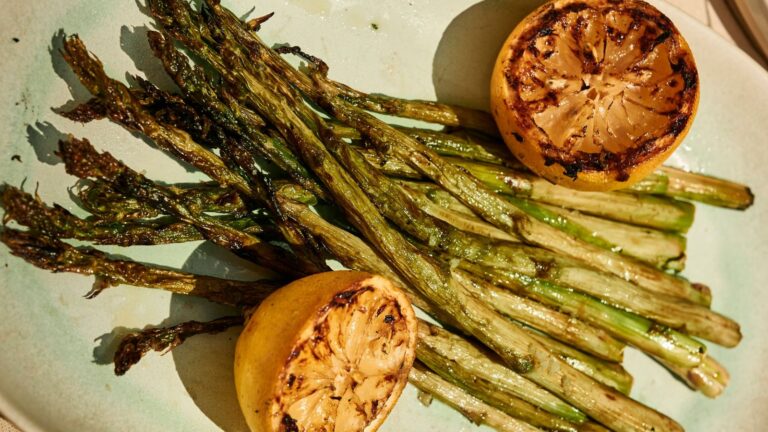 Grilled asparagus spears served on a plate with two charred lemon halves.