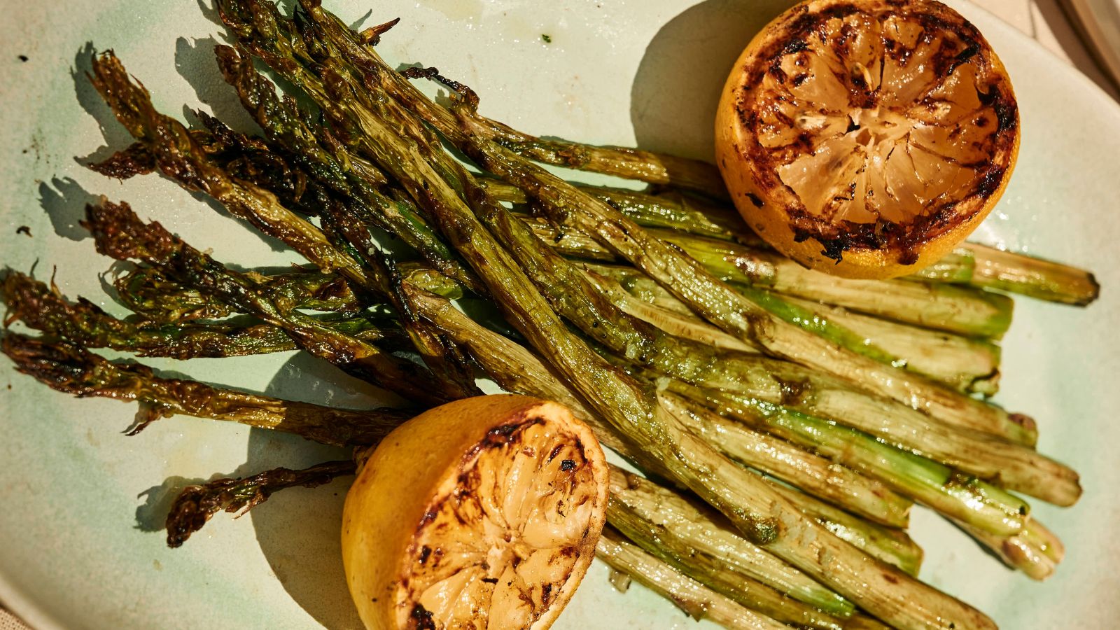 Grilled asparagus spears served on a plate with two charred lemon halves.