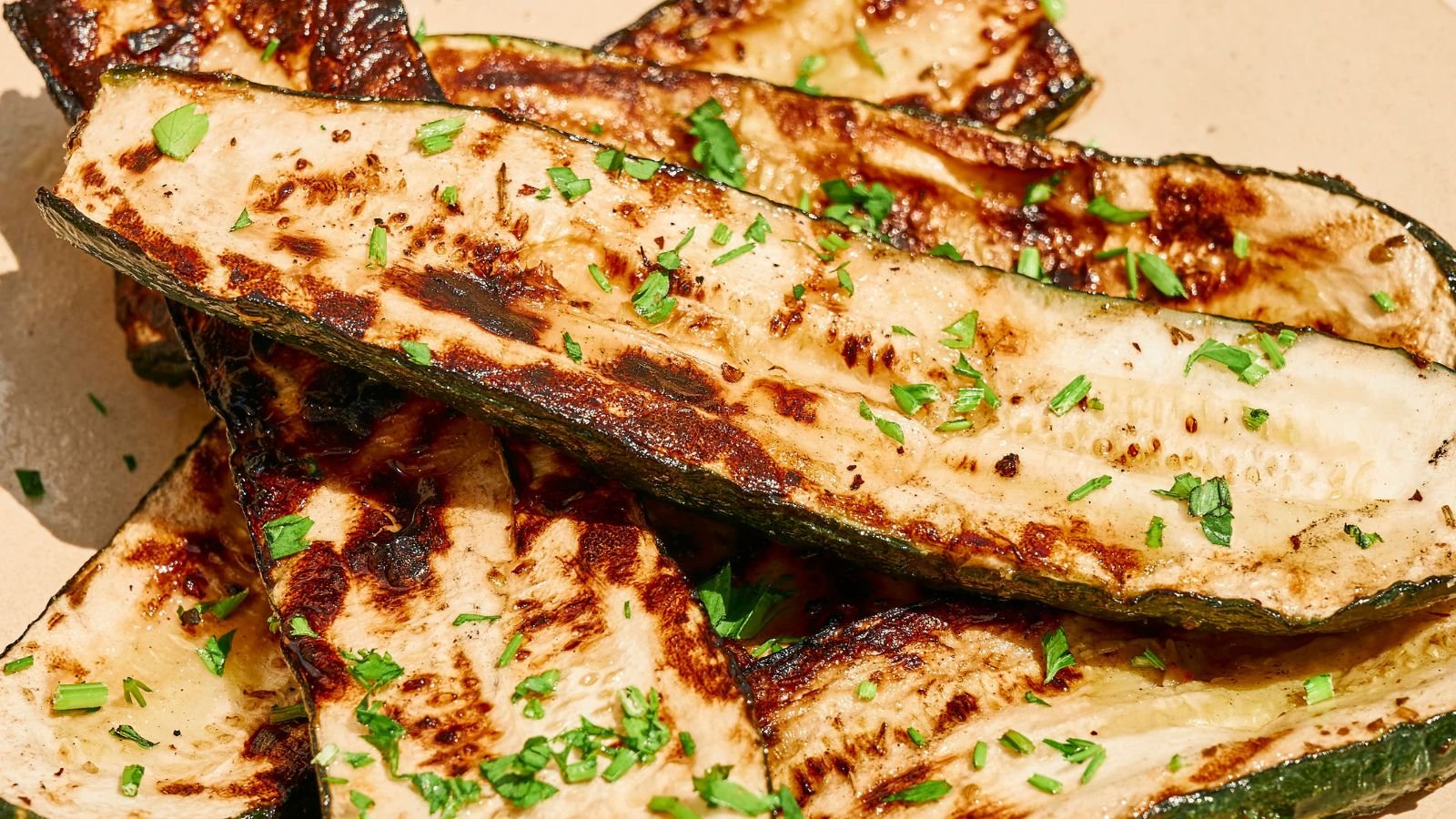 Grilled zucchini slices garnished with chopped herbs on a light-colored plate.