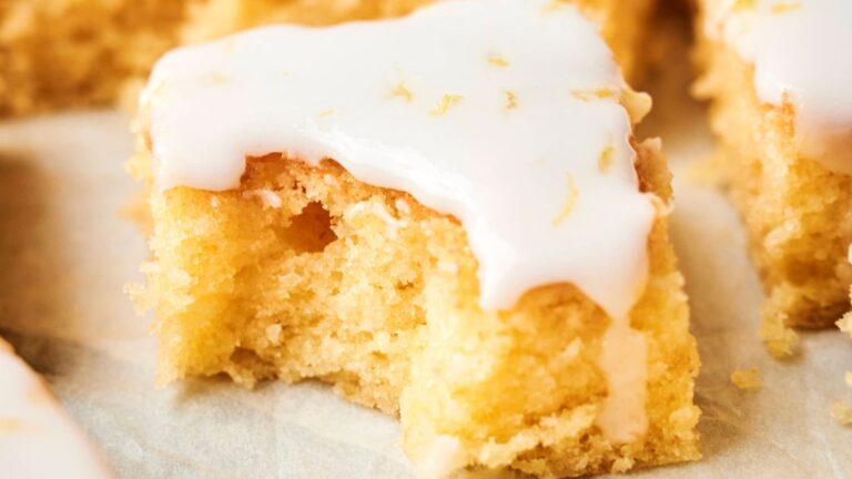 A close-up of a lemon drizzle cake square with white icing on top, showing its moist and airy texture.