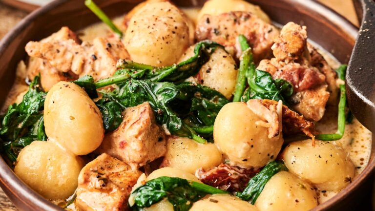 A bowl of gnocchi with pieces of chicken, wilted spinach, and sundried tomatoes in a creamy sauce.