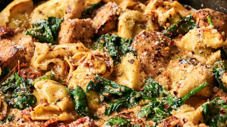 Tortellini pasta with spinach, sun-dried tomatoes, and chicken pieces in a creamy sauce, topped with grated cheese and seasonings.