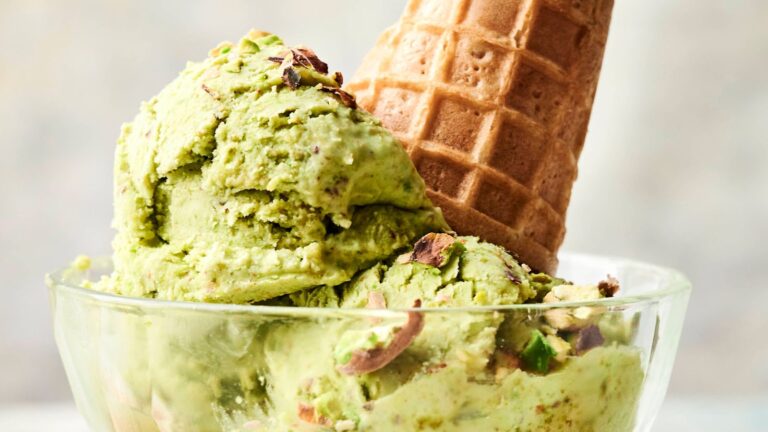 A glass bowl with two scoops of pistachio ice cream and an ice cream cone placed on top.