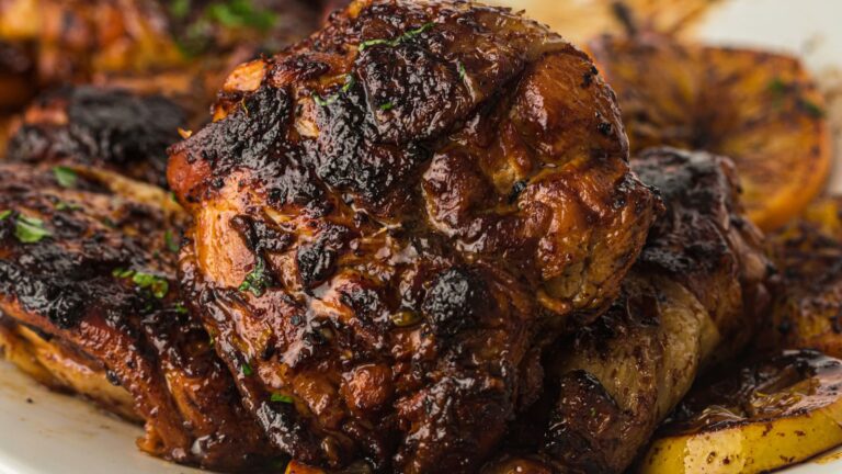 Close-up of a piece of grilled, charred meat with visible seasoning, resting on a plate with roasted potatoes and garnished with herbs.