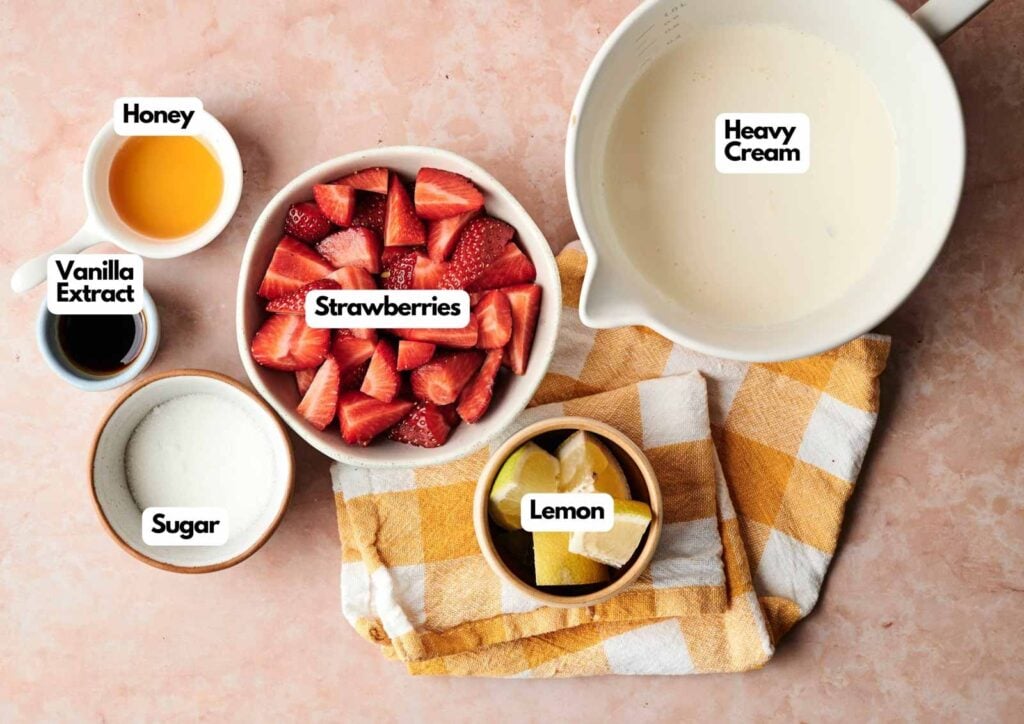 Bowls with labeled ingredients for Strawberry Ice Cream&mdash;heavy cream, strawberries, lemon, sugar, vanilla extract, and honey&mdash;on a pink surface with a yellow plaid cloth.