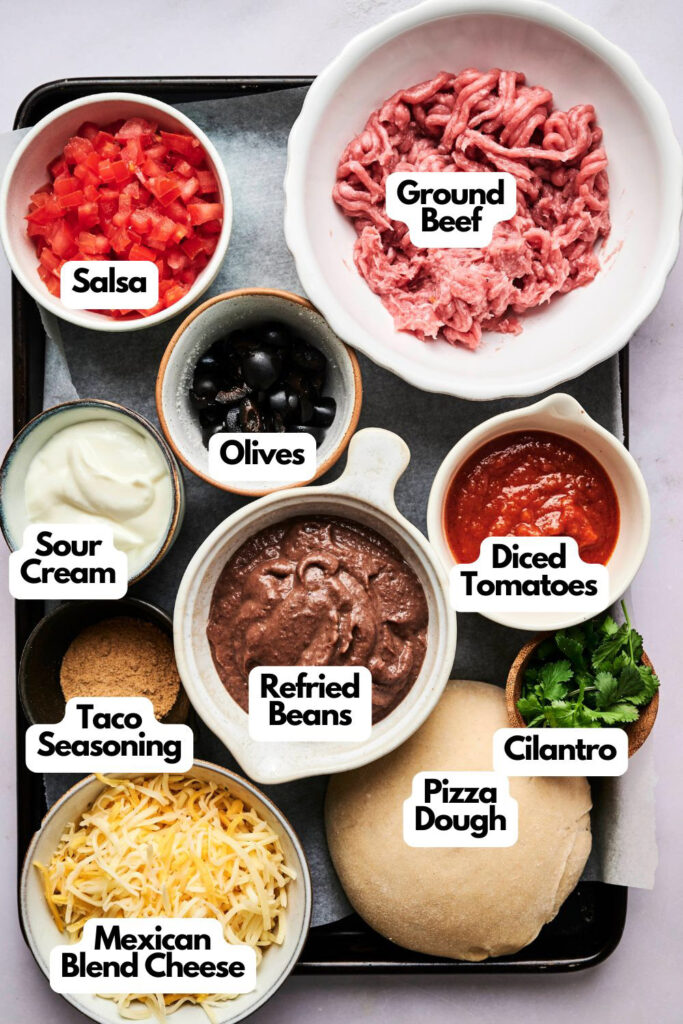 A tray with bowls containing ground beef, salsa, olives, sour cream, taco seasoning, Mexican blend cheese, refried beans, pizza dough, diced tomatoes, and cilantro&mdash;perfect ingredients for a flavorful taco pizza.