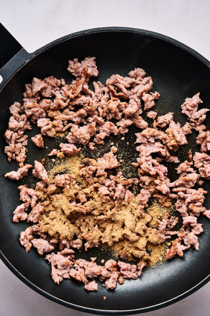 Ground meat sizzles in a black skillet, seasoned to perfection—ideal for topping a flavorful taco pizza.