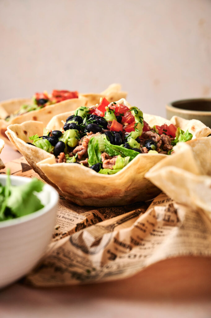 Enjoy our classic Taco Salad served in an edible tortilla bowl, filled with lettuce, beans, ground meat, tomatoes, and avocado. A side of cilantro and extra tortillas make this Taco Salad a flavorful meal.
