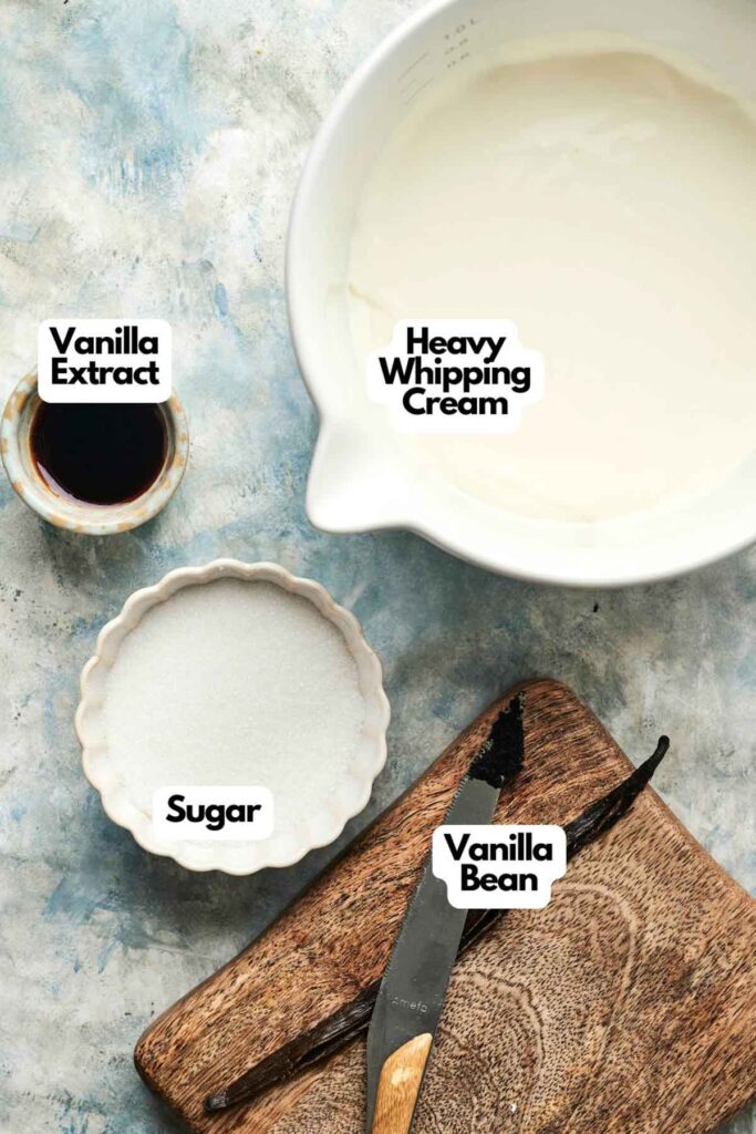 A bowl of heavy whipping cream, sugar, vanilla extract, and a vanilla bean rest on a wooden board&mdash;ingredients ready to be transformed into creamy homemade Vanilla Ice Cream on a textured surface.
