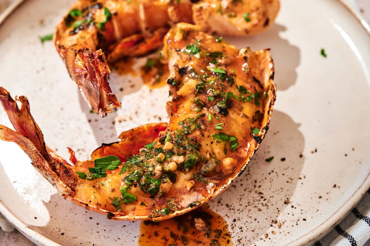 Grilled Lobster Tail served on a white plate, topped with garlic herb butter sauce and garnished with chopped parsley for an elegant seafood dish.