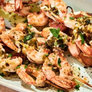 Grilled shrimp skewers, garnished with chopped herbs and seasoning, are served on a light-colored platter for a fresh and flavorful grilled shrimp dish.