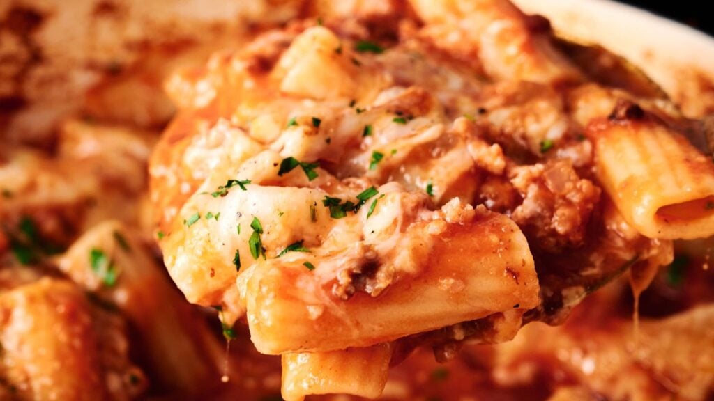 Close-up of baked rigatoni pasta with melted cheese, ground meat, tomato sauce, and sprinkled herbs.
