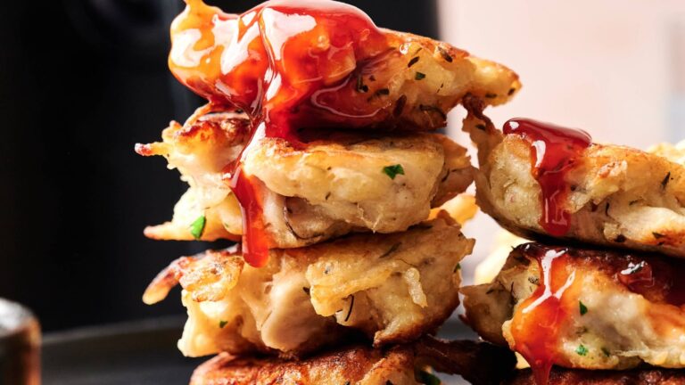 A close-up of stacked crispy fritters topped with a glossy red sauce, showing texture and detail.