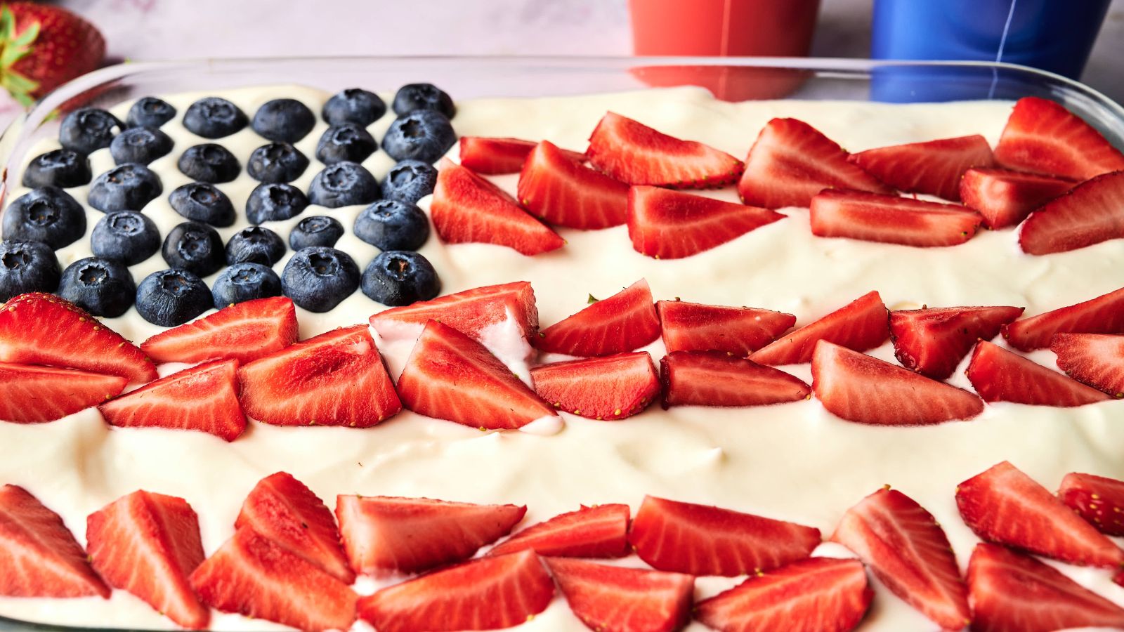 A dessert tray decorated like an American flag with blueberries in the top left corner and sliced strawberries arranged in rows on a white creamy base.