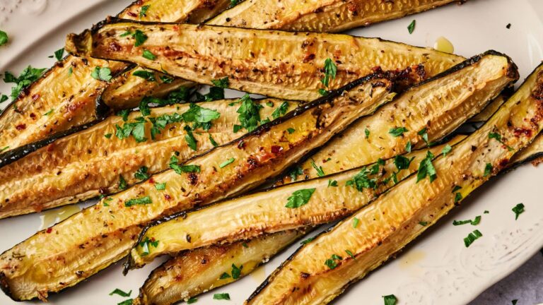 Roasted zucchini halves garnished with chopped fresh parsley, arranged on a white plate.