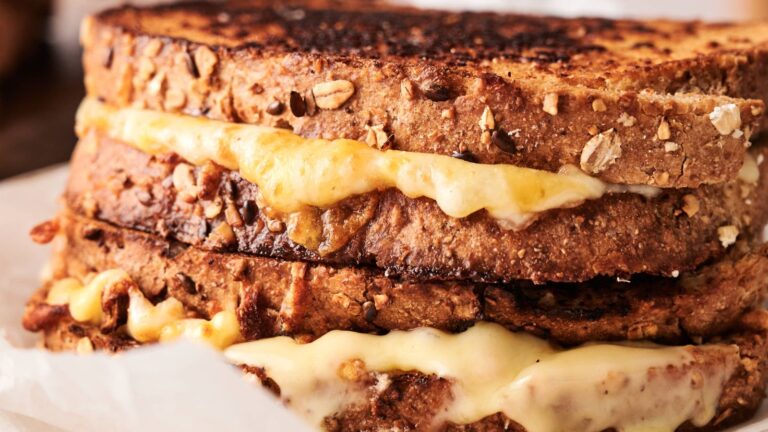 Close-up of two grilled cheese sandwiches made with multigrain bread, showing melted cheese oozing between the toasted slices.