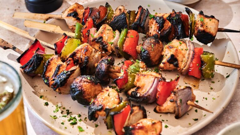 Grilled chicken and vegetable skewers with charred edges served on a white plate, garnished with chopped herbs.