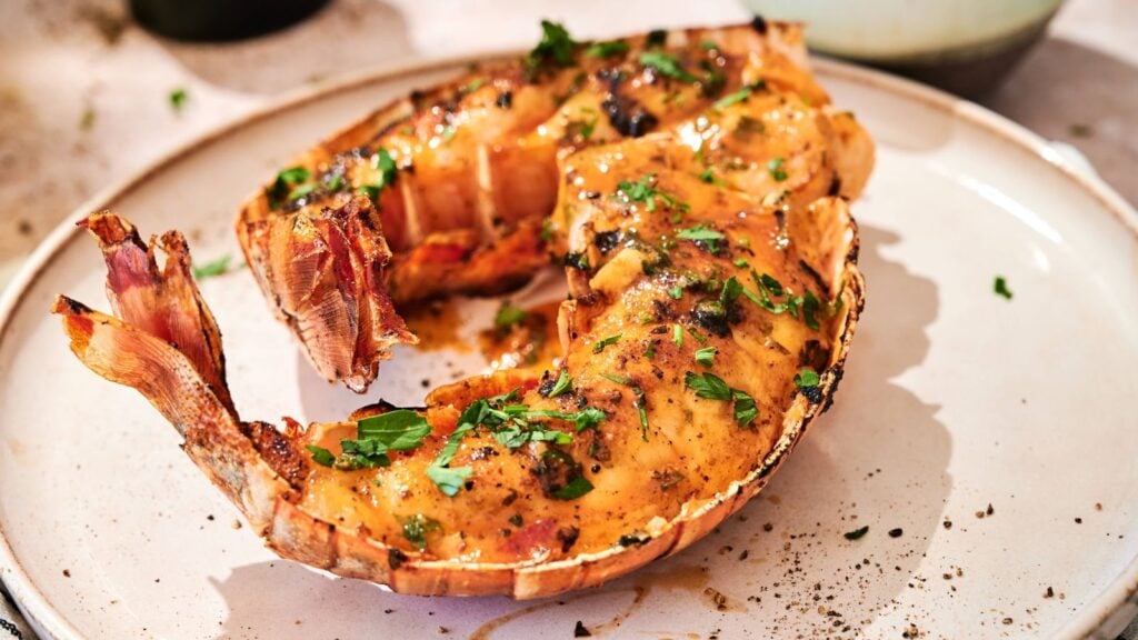 Cooked lobster tail with herbs and seasoning served on a white plate.