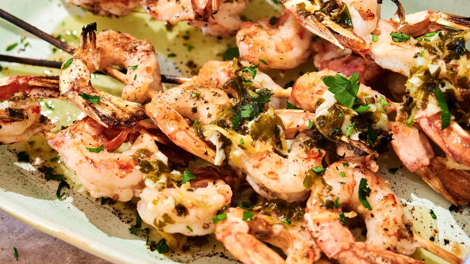 Grilled shrimp skewers served on a plate, topped with chopped herbs and a drizzle of sauce.