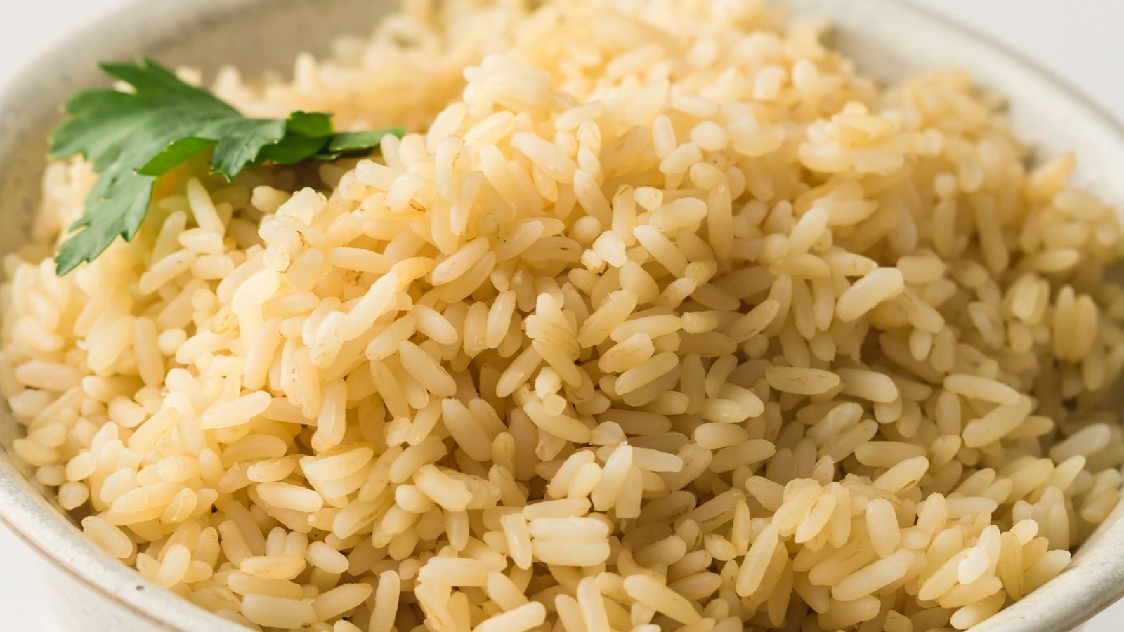A bowl of cooked brown rice topped with a sprig of fresh parsley.