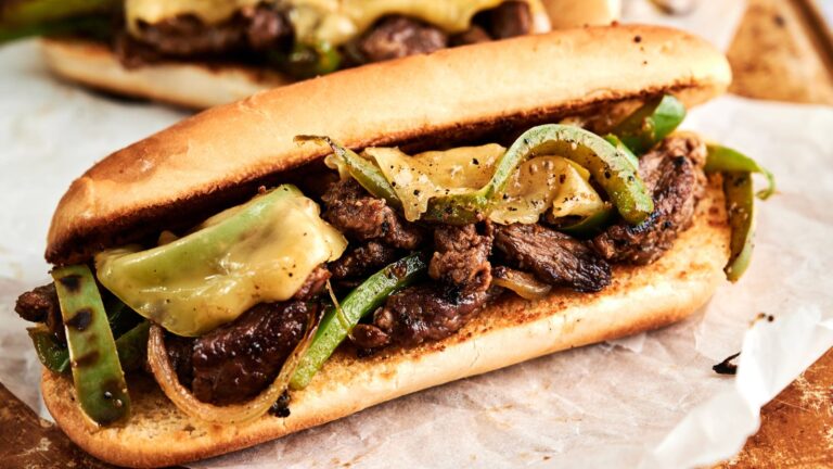 A sandwich filled with grilled beef, melted cheese, green bell peppers, and onions on a toasted hoagie roll.