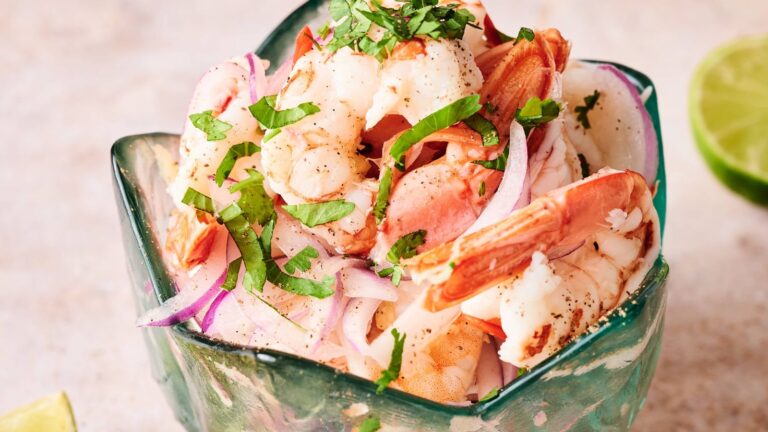 A glass bowl filled with shrimp, sliced red onions, and chopped cilantro, with a lime on the side.