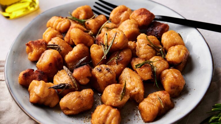 Plate of golden-brown gnocchi garnished with sprigs of rosemary, served on a gray dish with a black fork.
