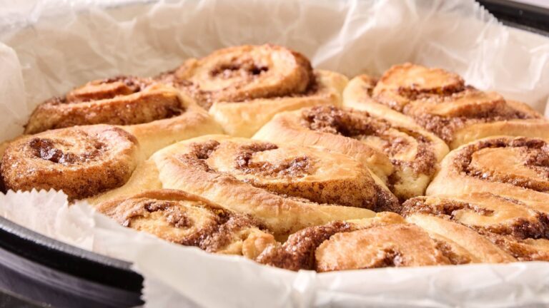 A close-up view of freshly baked cinnamon rolls arranged in a round pan lined with parchment paper.
