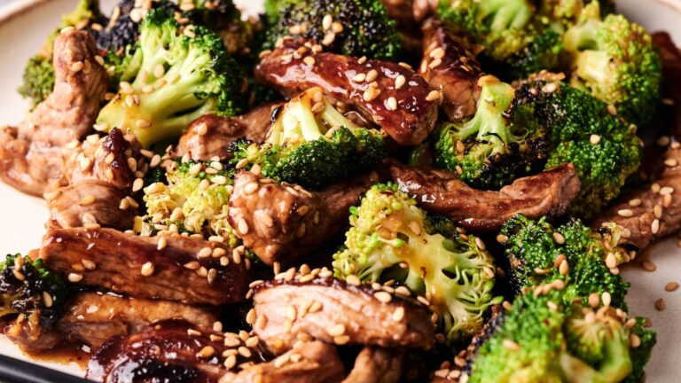 Stir-fried beef strips with broccoli florets, coated in a brown sauce and topped with sesame seeds, served on a plate.