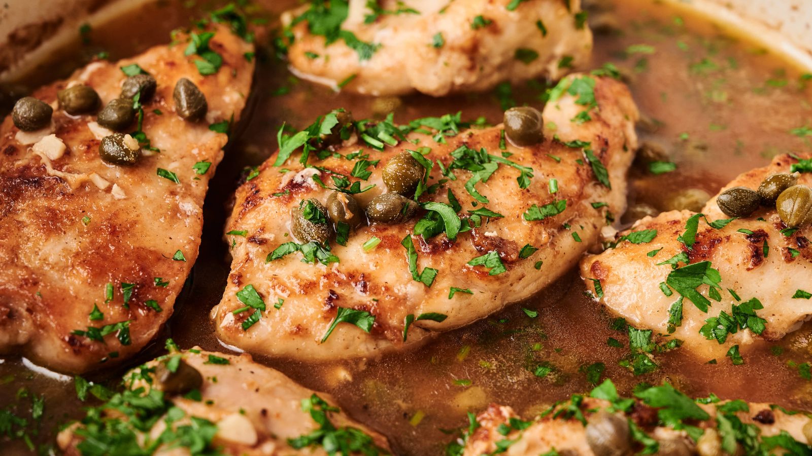 Chicken breasts simmering in a brown sauce, topped with capers and chopped fresh herbs.
